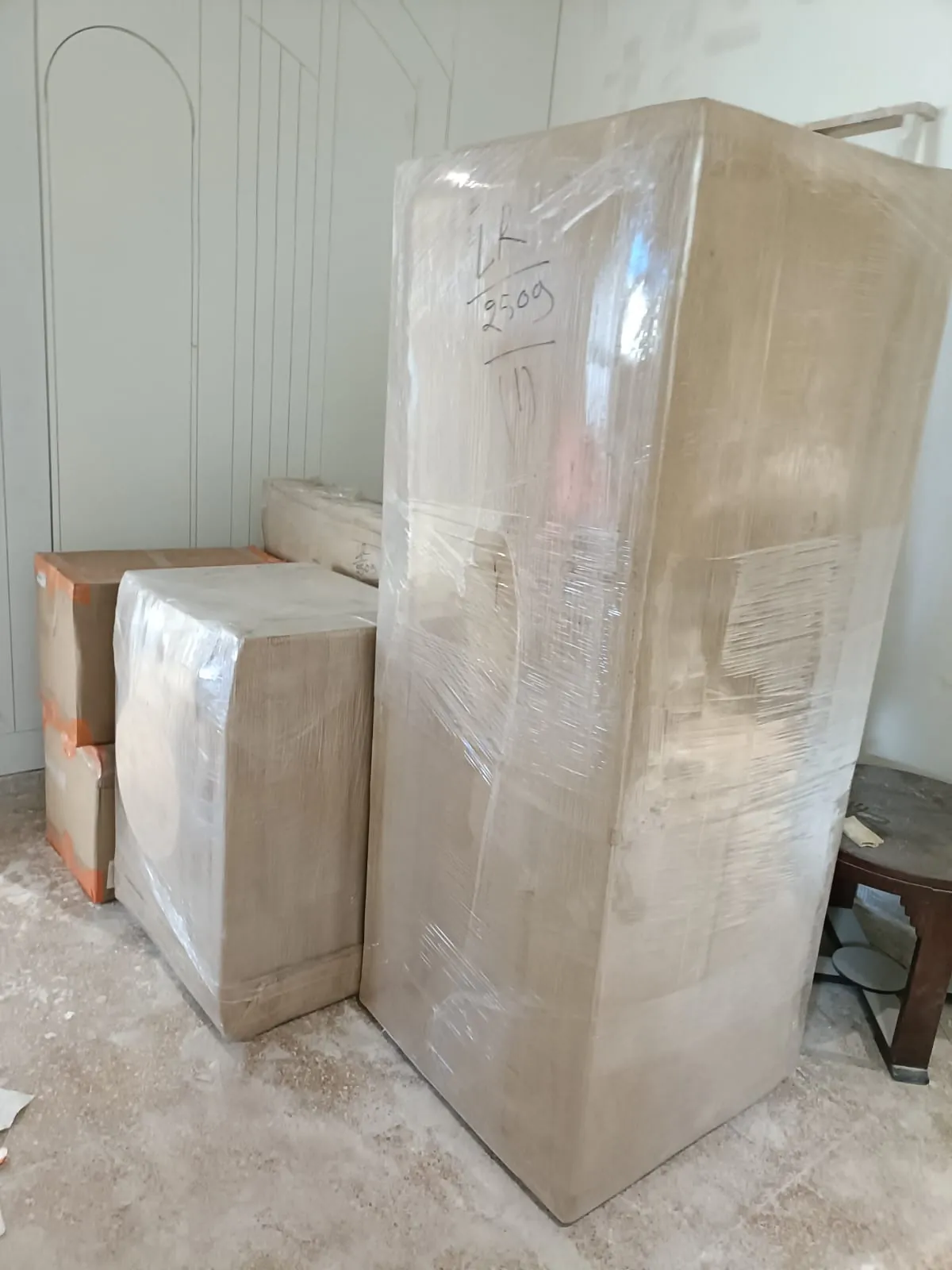 Tall shrink-wrapped wardrobe with a lot number beside packed cartons in an empty room