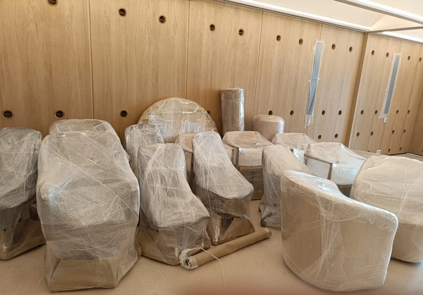 Rows of lounge chairs and tables wrapped in stretch film in an office with wooden wall panels